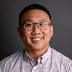 a man wearing glasses and a plaid shirt is smiling for the camera .